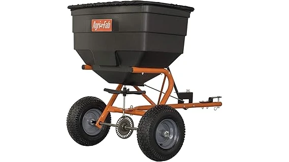 The image shows a pull-behind fertilizer spreader attached to a tractor, ready for lawn care.